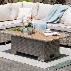 a couch and table on a patio with flowers in vases next to the coffee table