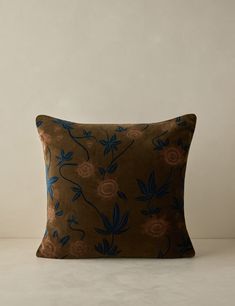 a brown pillow with blue and pink flowers on the front, sitting on a white surface