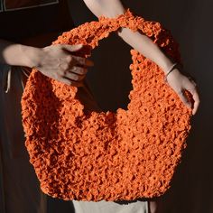 an orange crocheted bag being held by two hands