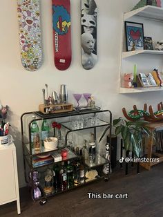 there are three skateboards mounted on the wall above this bar cart, and two shelves with liquor bottles