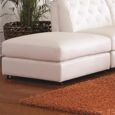 a white sectional couch sitting on top of a wooden floor next to a potted plant