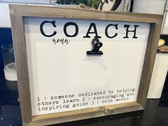 a sign that says coach written in black ink on a white board next to a potted plant