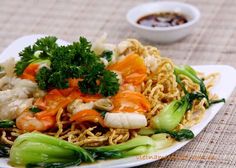 a white plate topped with noodles and vegetables next to a bowl of dipping sauce on a table