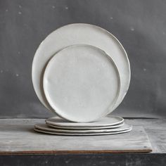 four white plates stacked on top of each other in front of a gray wall and floor