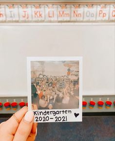 a person holding up a polaroid photo in front of a wall with writing on it