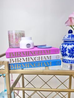 a table topped with three books and a vase filled with flowers next to a pink rose