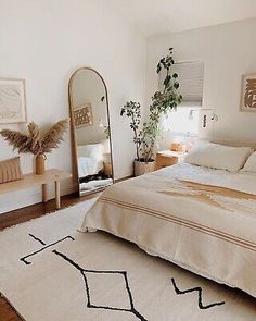 a bedroom with a bed, mirror and plant on the floor in front of it