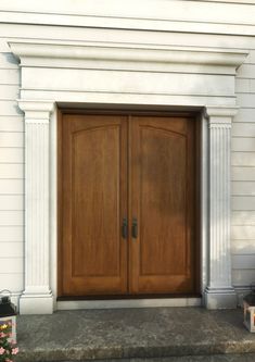 two wooden doors sitting on the side of a white building next to a flower pot