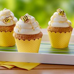 three cupcakes with white frosting and honeybee decorations on a tray outside