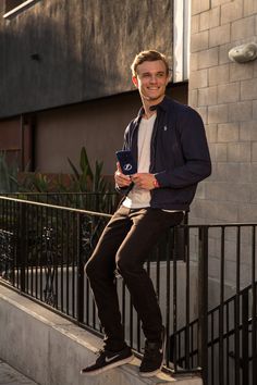 a man sitting on top of a metal rail next to a building with a cell phone in his hand