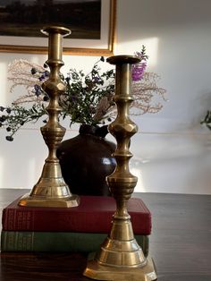 two brass candlesticks on top of books in front of a vase with flowers