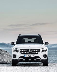 the front end of a white mercedes gls parked on top of a rocky beach