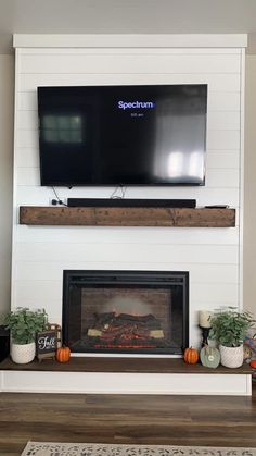 a flat screen tv mounted above a fireplace with potted plants on the mantel