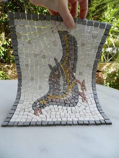 a hand is holding up a mosaic tile piece