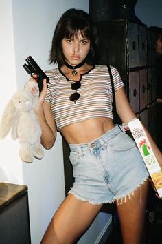 a young woman holding a bottle and a teddy bear in her hand while standing next to a dresser