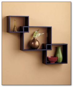 three square shelves with vases and other items on them against a tan colored wall