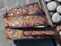 two brown leather belts sitting next to each other on top of a stone floor covered in stones