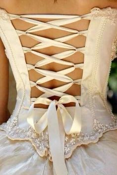 the back of a woman's wedding dress with white ribbons and bows on it