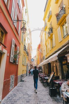 a man walking down a street next to tall buildings with people sitting at tables in front of them