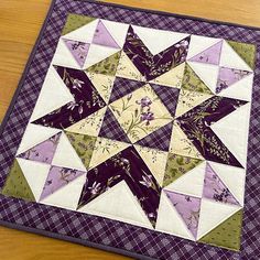 a quilted table topper with purple and green flowers in the center on a wooden surface