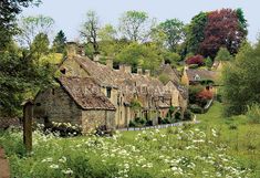 an old stone house in the middle of a field with flowers and trees around it