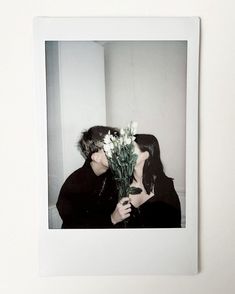 a couple kissing each other while holding flowers in front of their face and the photo is framed on a wall