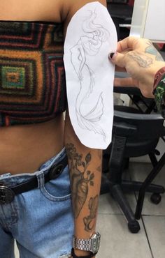 a woman with tattoos on her arm holding a piece of paper in front of her stomach