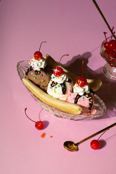 an ice cream sundae with cherries and whipped cream in a banana boat on a pink surface