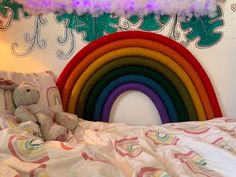 a stuffed animal sitting on top of a bed next to a rainbow wall hanging above it