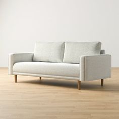 a white couch sitting on top of a hard wood floor next to a wall in an empty room