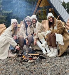 four women sitting around a campfire in front of a cabin