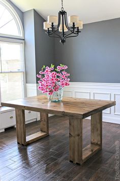 a wooden table sitting on top of a hard wood floor next to a vase with flowers