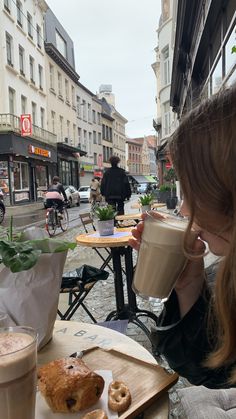 a woman drinking coffee and eating doughnuts at an outdoor cafe in the city