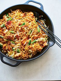 a skillet filled with noodles and meat on top of a white table next to chopsticks