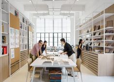 three people standing around a table in a room with bookshelves and shelving