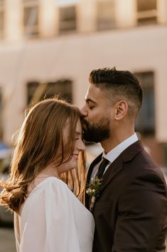 a man and woman standing next to each other in front of a building with their faces close together