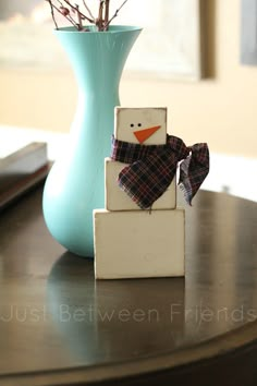 a wooden block snowman sitting on top of a table next to a blue vase