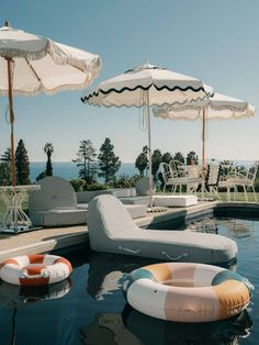 an outdoor swimming pool with lounge chairs, umbrellas and inflatable rafts