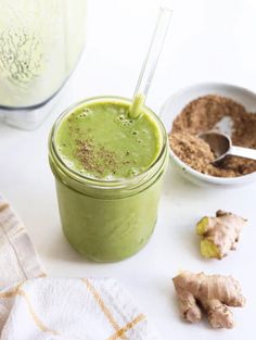 a green smoothie in a mason jar next to ginger and powdered sugar on a white surface