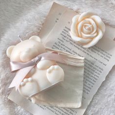 two white teddy bears sitting on top of an open book next to a pink rose