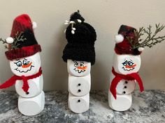 three snowmen made out of toilet paper rolls and some fake pine branches with hats on them