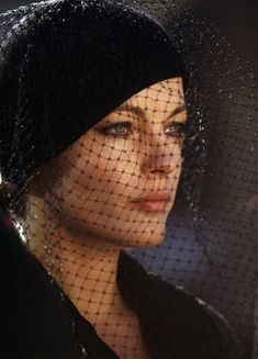 a woman wearing a black hat with a veil over her head and looking off to the side