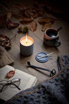 an open book, eyeglasses, and candle on a table with autumn leaves