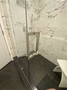 a glass shower door in a bathroom with marble walls and flooring on the wall