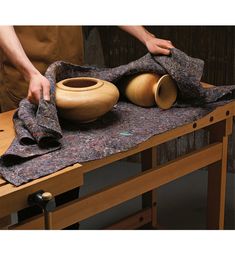 a person is working on a wooden table with two vases and a cloth draped over it