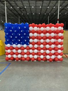 an american flag made out of red, white and blue balloons is displayed in a warehouse