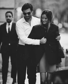 a man and woman are walking down the street with their arms wrapped around each other