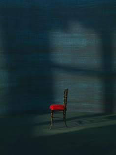 a red chair sitting in the middle of a room next to a wall with a shadow cast on it