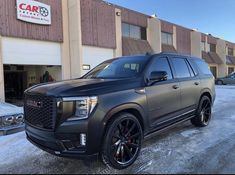 a black suv parked in front of a car dealership with snow on the ground