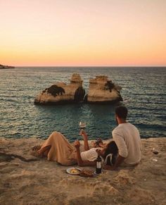 two people sitting on the beach drinking wine